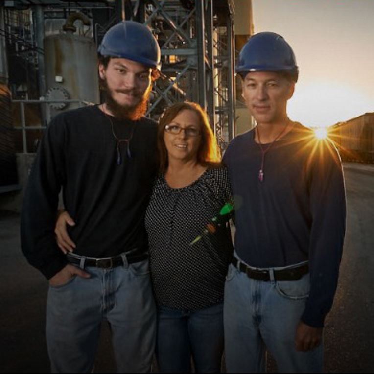 Two males in hardhats with arms around woman 