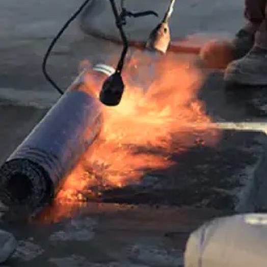 Contractor on a commercial roof using fire to install asphaltic roof