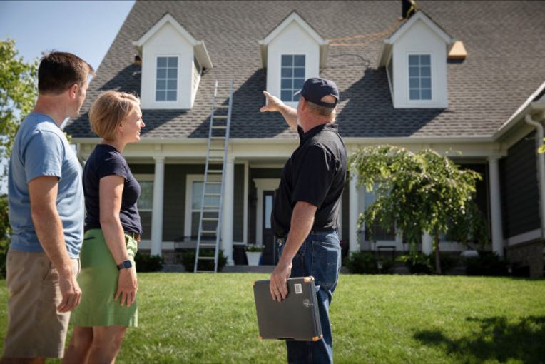 Contractor outside home pointing at roof with homewoners