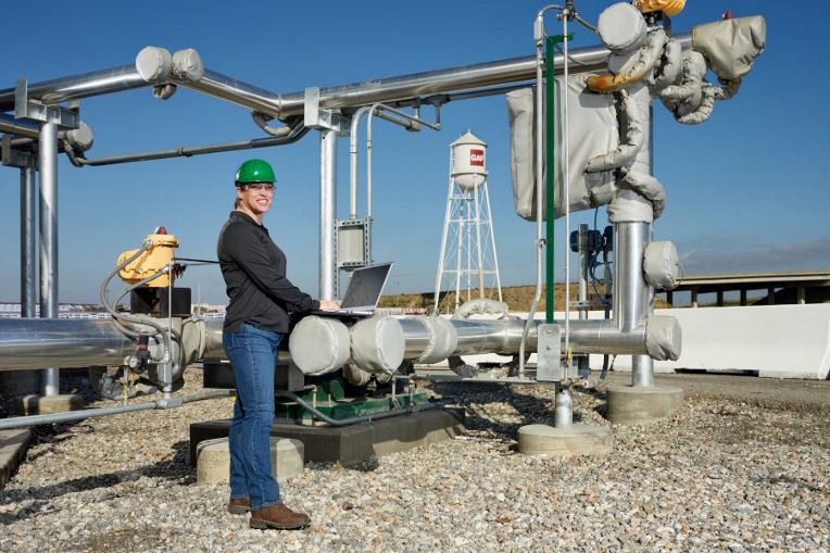 Female GAF employee supervising machinery outside roofing plant"