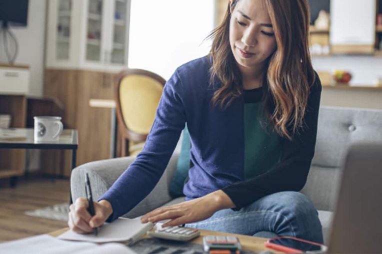 Woman using a calculator and paper to calculate cost of a new roof 