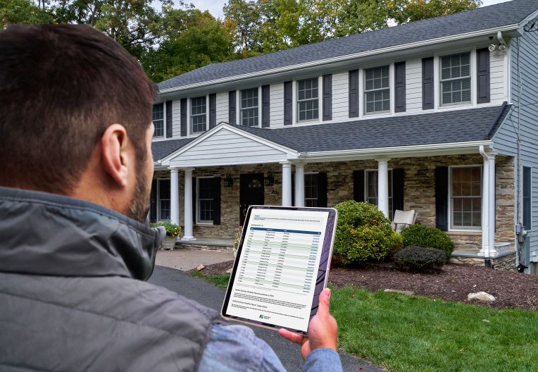 Contractor holding tablet in front of home open to QuickSite property data reports from GAF