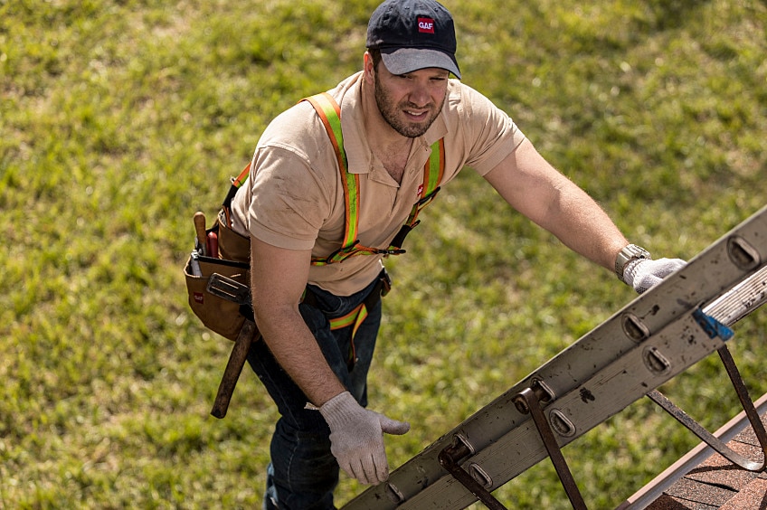 Roofer climbing a ladder leaning against the roof of a house.