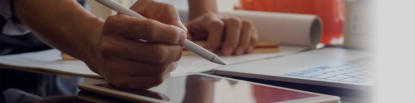 Hand holding pen writing on tablet