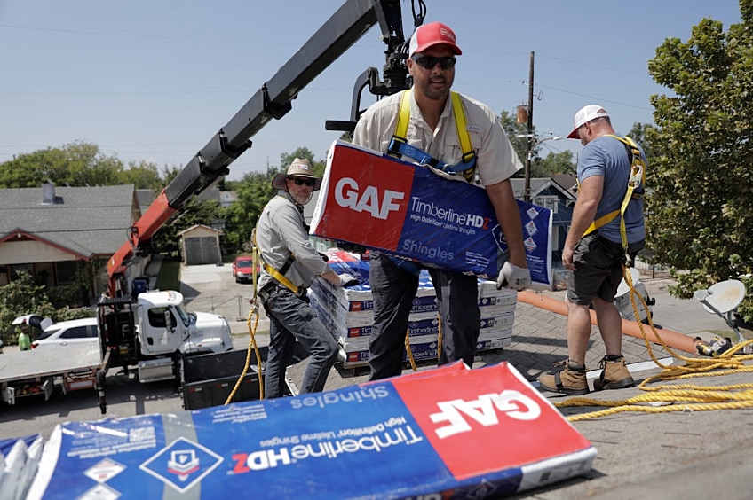 A roofer unloads shingles on to the roof of a house prior to installing them