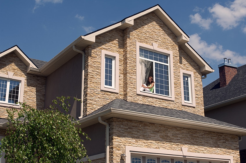 Woman sitting in open window under steep-slope shingle roof