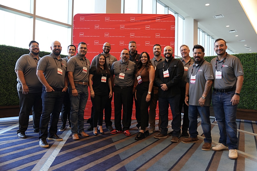 A smiling group of men and women gather in front of a red expo backdrop for a photo.