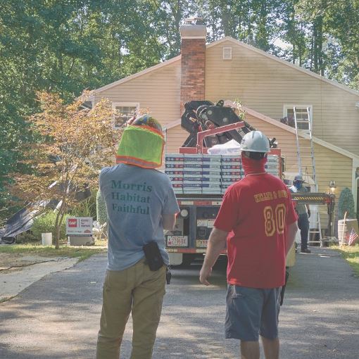 Two members of the community watching GAF donate materials for a new roof.