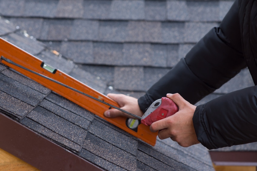 man on ladder measuring roof with level