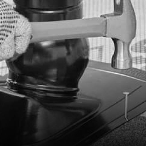 Shaded image of a GAF roofer’s gloved hands using a hammer and nail to install Master Flow pivot pipe boot flashing to a residential roof