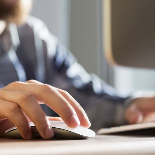 A person in front of a computer clicking on a mouse.