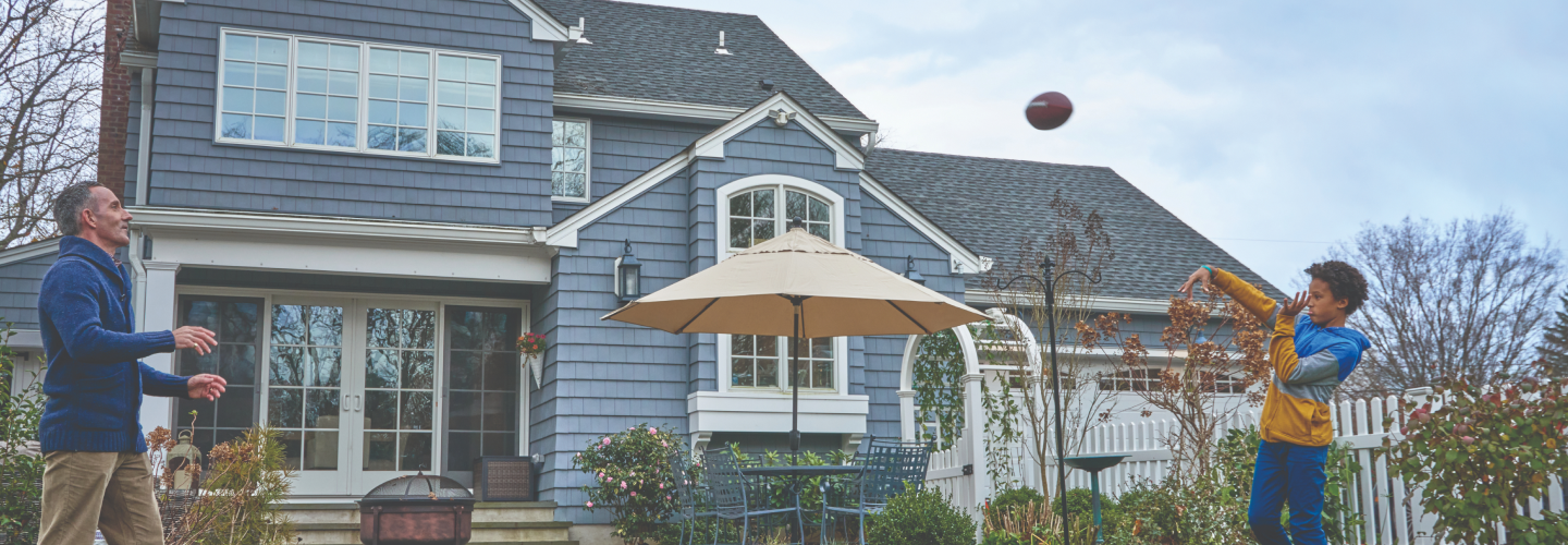 Man and boy catching football outside of a home with a GAF roof